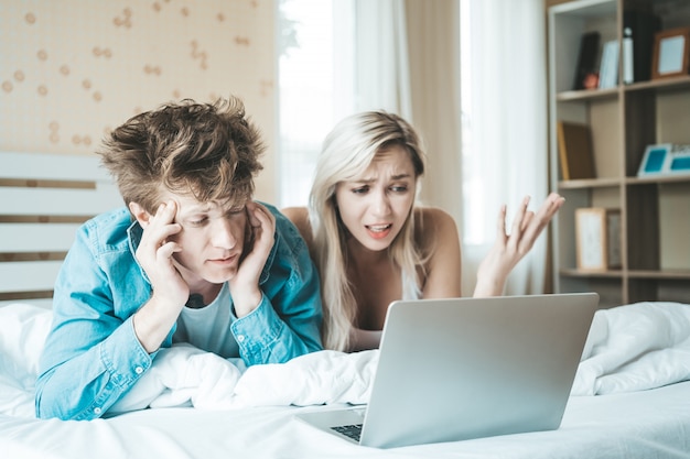 Coppie felici che per mezzo del computer portatile sul letto