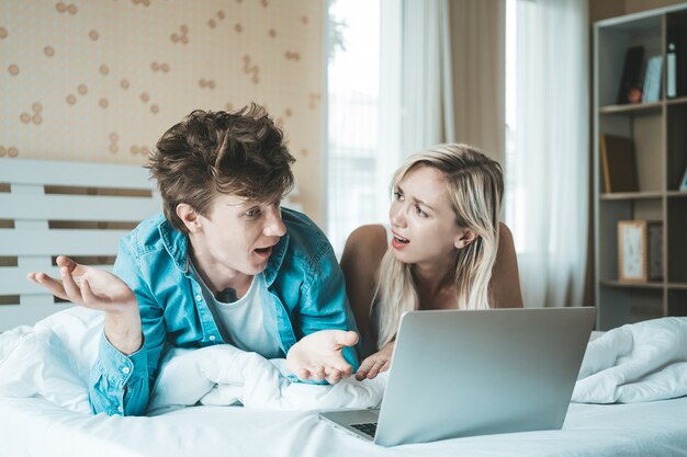 Coppie felici che per mezzo del computer portatile sul letto