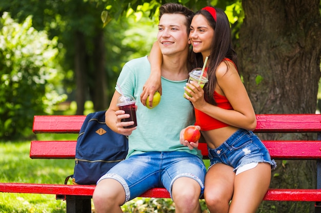 Coppie felici che tengono frutta sana e frullati godendo nel parco