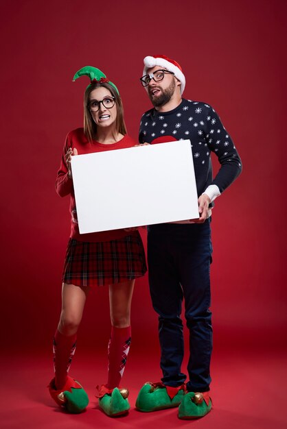 Coppie felici del nerd in vestiti di Natale che tengono documento in bianco