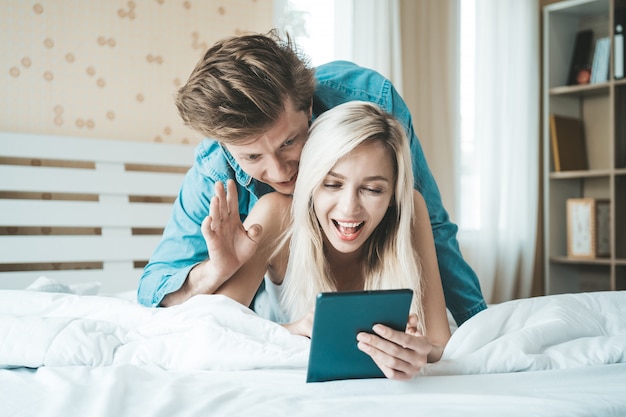 Coppie felici facendo uso del computer della compressa sul letto