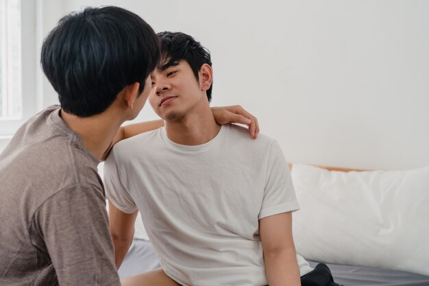 Coppie gay asiatiche che baciano sul letto a casa. I giovani asiatici LGBTQ + uomini felici si rilassano insieme riposano insieme trascorrono momenti romantici dopo essersi svegliati in camera da letto a casa la mattina.