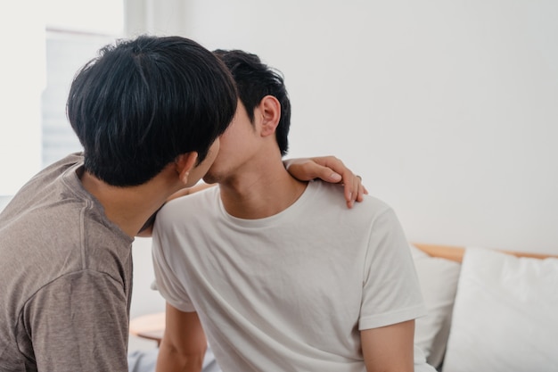 Coppie gay asiatiche che baciano sul letto a casa. I giovani asiatici LGBTQ + uomini felici si rilassano insieme riposano insieme trascorrono momenti romantici dopo essersi svegliati in camera da letto a casa la mattina.