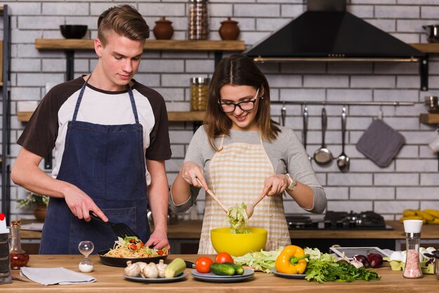 Coppie in grembiuli che cucinano alimento in cucina