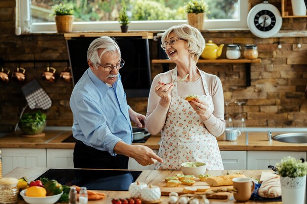 Coppie mature felici che parlano e che si divertono mentre preparano il cibo in cucina