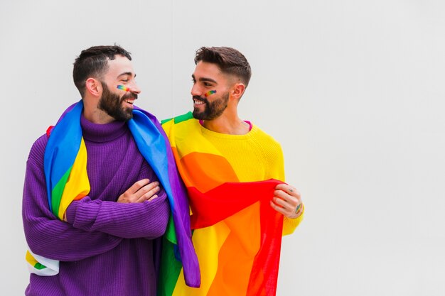 Coppie omosessuali con le bandiere LGBT sulle spalle che sorridono insieme