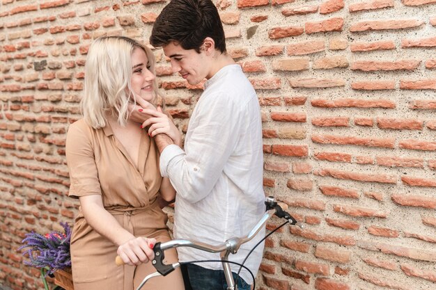 Coppie romantiche che posano contro il muro di mattoni con la bicicletta