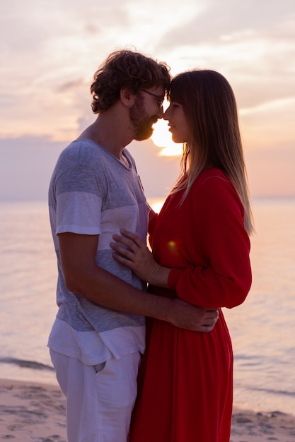 Coppie romantiche felici sulla spiaggia tropicale al tramonto.