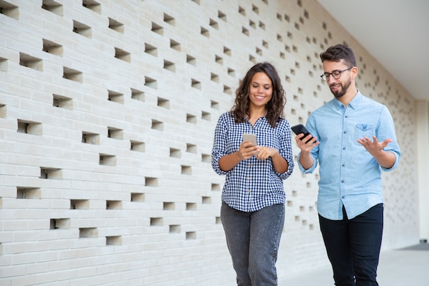 Coppie sorridenti che camminano e che per mezzo degli smartphones