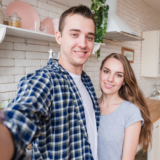 Coppie sorridenti che prendono selfie in cucina
