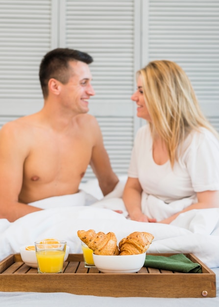 Coppie sorridenti che si siedono sul letto vicino al cibo sul tavolo della colazione