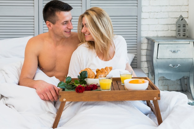 Coppie sorridenti che si siedono sul letto vicino alla prima colazione a bordo