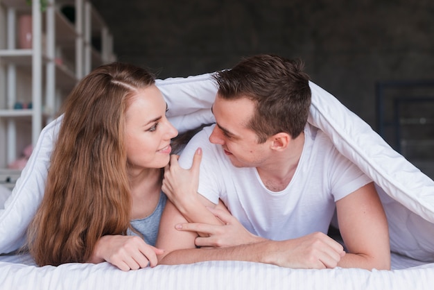 Coppie sorridenti che si trovano sul letto sotto il piumone