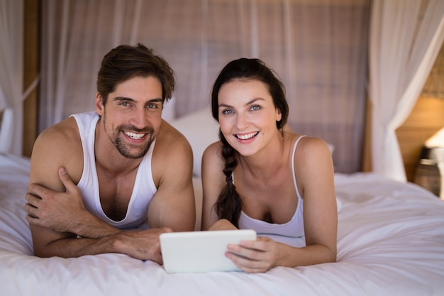 Coppie sorridenti facendo uso della compressa digitale sul letto nel cottage