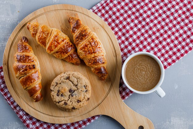 Cornetti con caffè, biscotti, tagliere distesi su intonaco e panno da picnic