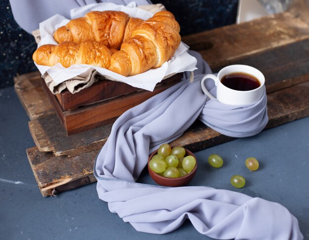 Cornetti e uva verde con una tazza di caffè espresso sul tavolo blu