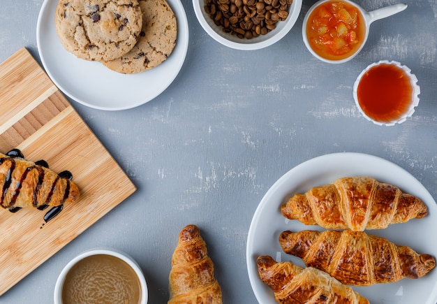 Cornetti in un piatto con caffè, fagioli, biscotti, marmellata, miele piatto disteso