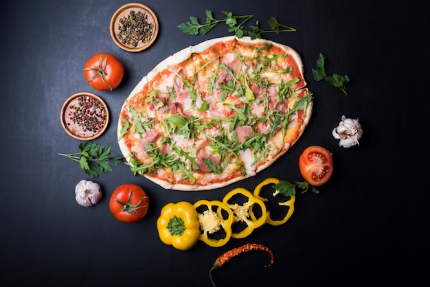 Cornice circolare fatta di ingredienti freschi intorno deliziosa pizza italiana sul bancone nero