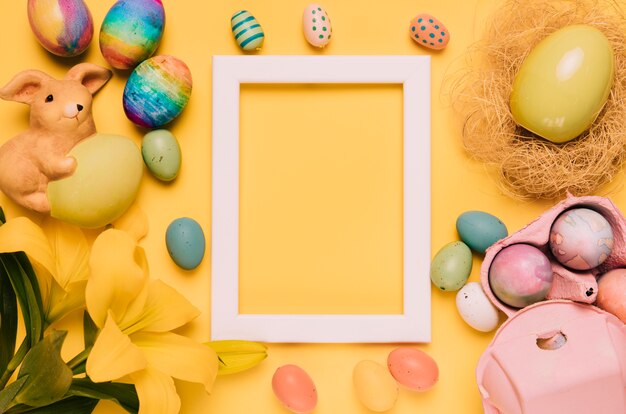 Cornice vuota bordo bianco decorato con uova di Pasqua; fiore di giglio e nido su sfondo giallo