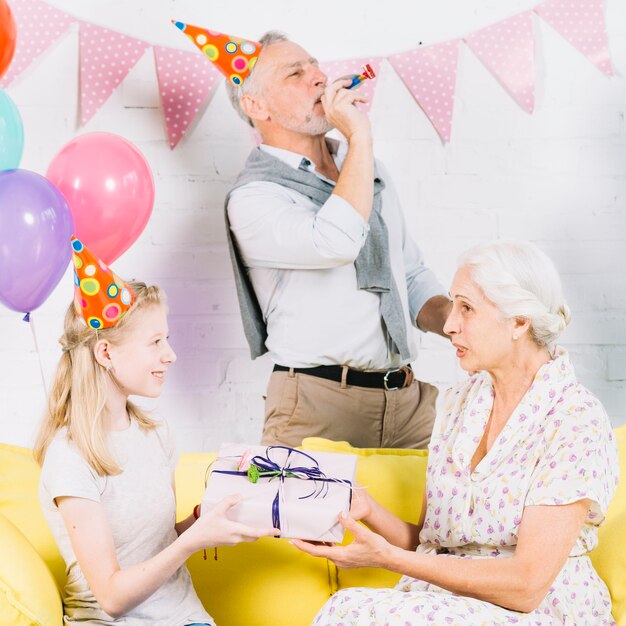 Corno di partito di salto dell&#39;uomo mentre ragazza che dà il regalo di compleanno a sua nonna