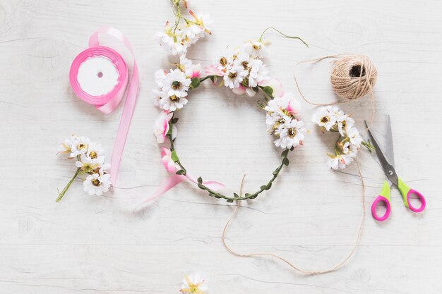 Corona floreale bianca e rosa con nastro rosa; rocchetto e forbici sul tavolo