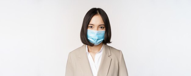 Coronavirus e concetto di posto di lavoro Ritratto di donna d'affari asiatica d'affari in maschera medica che guarda lo sfondo bianco della fotocamera