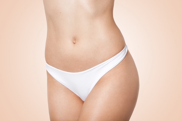 corpo sottile di donna in lingerie bianca su beige, femmina con figura perfetta che mostra la sua pancia piatta e liscia