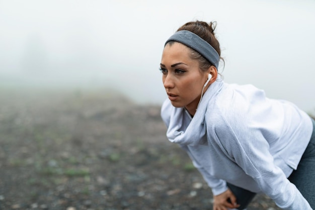 Corridore femminile che riprende fiato e si prende una pausa dopo aver fatto jogging nella natura con tempo nebbioso Copia spazio