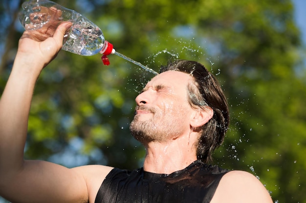 Corridore fitness che beve e spruzza acqua in faccia Immagine divertente di un bel maschio rinfrescante durante l'allenamento