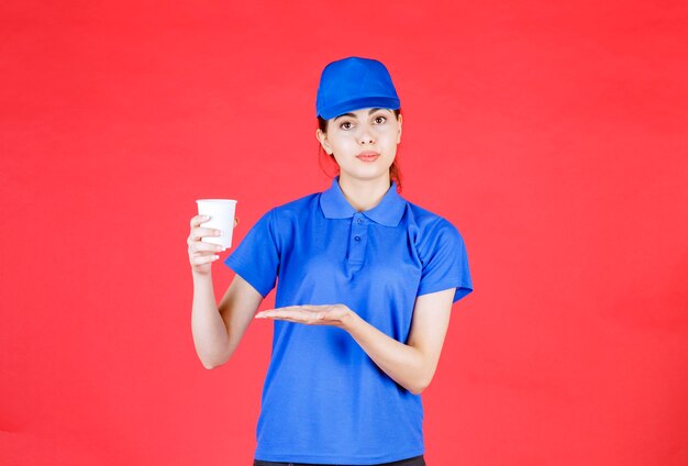 Corriere della bella donna in attrezzatura blu che tiene tazza di tè su colore rosso.