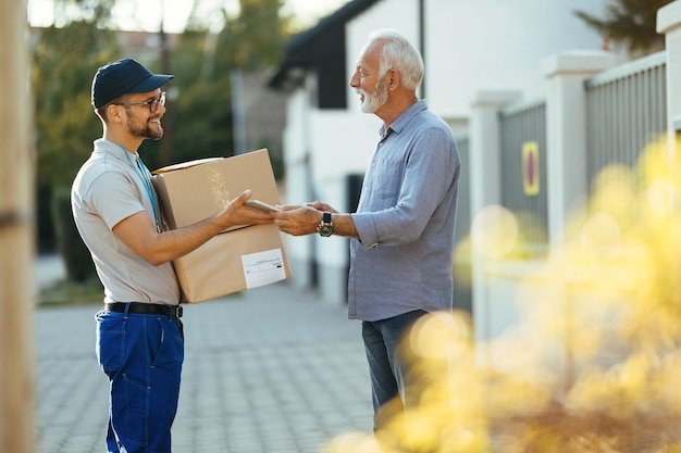 Corriere felice che dà il touchpad al cliente senior per cantare per una consegna a domicilio