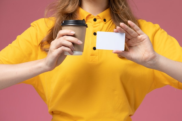 Corriere femmina giovane vista ravvicinata anteriore in uniforme gialla che tiene tazza di caffè e carta bianca su sfondo rosa lavoratore di servizio di consegna uniforme di lavoro scrivania