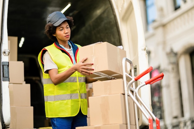 Corriere femminile afroamericano che scarica i pacchi dal camion di consegna