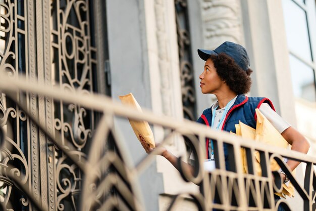 Corriere femminile afroamericano con pacchi alla porta d'ingresso dell'edificio residenziale