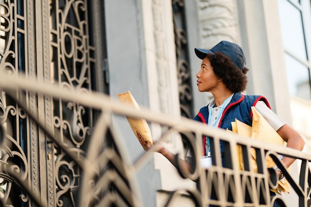 Corriere femminile afroamericano con pacchi alla porta d'ingresso dell'edificio residenziale