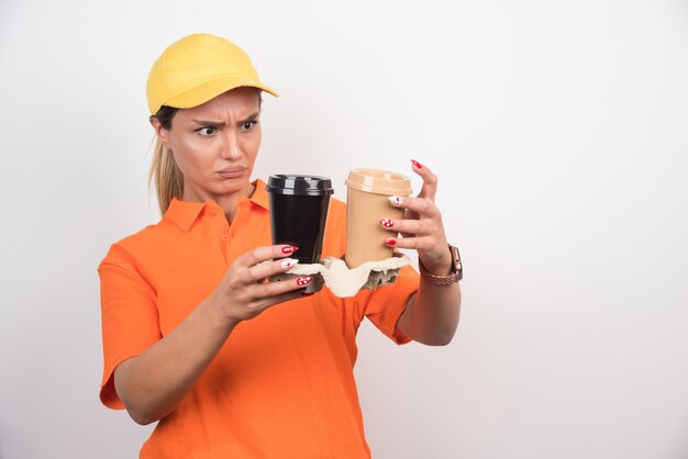 Corriere femminile biondo che esamina due tazze di caffè sulla parete bianca.