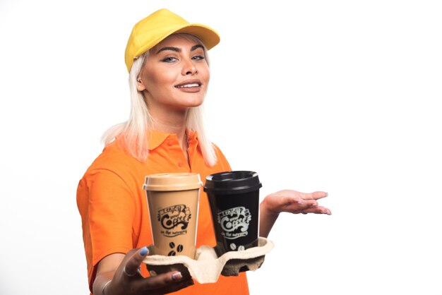 Corriere femminile che tiene due tazze di caffè su fondo bianco mentre sorride. Foto di alta qualità
