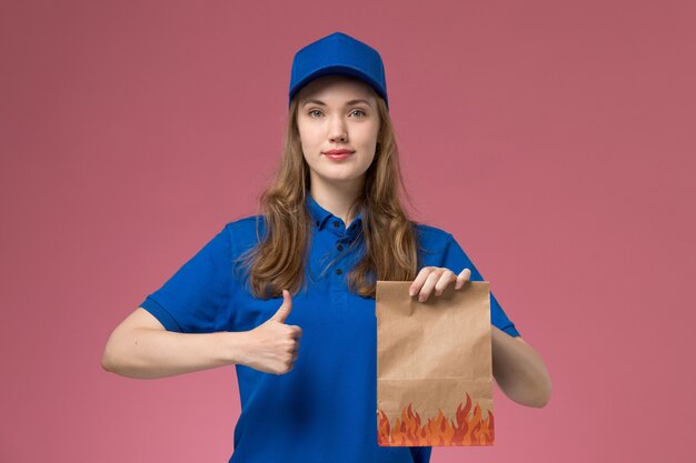 Corriere femminile di vista frontale in uniforme blu che tiene il pacchetto dell'alimento sull'azienda dell'uniforme di servizio del lavoratore di lavoro dello scrittorio rosa chiaro