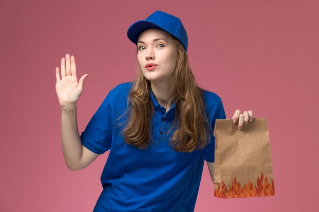 Corriere femminile di vista frontale in uniforme blu che tiene il pacchetto dell'alimento sull'azienda dell'uniforme di servizio dell'operaio di lavoro della scrivania rosa