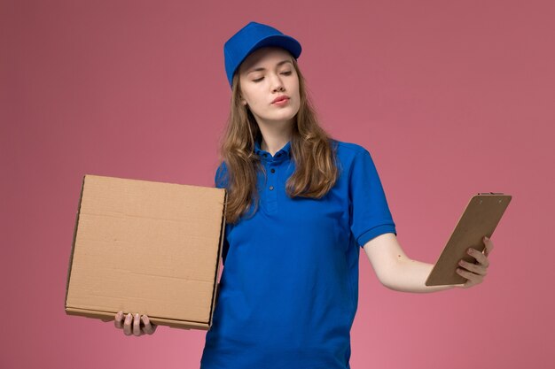 Corriere femminile di vista frontale in uniforme blu che tiene la scatola di consegna del cibo e il blocchetto per appunti sul lavoratore della compagnia di lavoro uniforme di servizio scrivania rosa