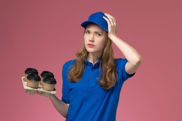 Corriere femminile di vista frontale in uniforme blu che tiene le tazze di caffè marroni di consegna che tengono la sua testa sul lavoratore dentellare dell'azienda dell'uniforme di servizio dello scrittorio