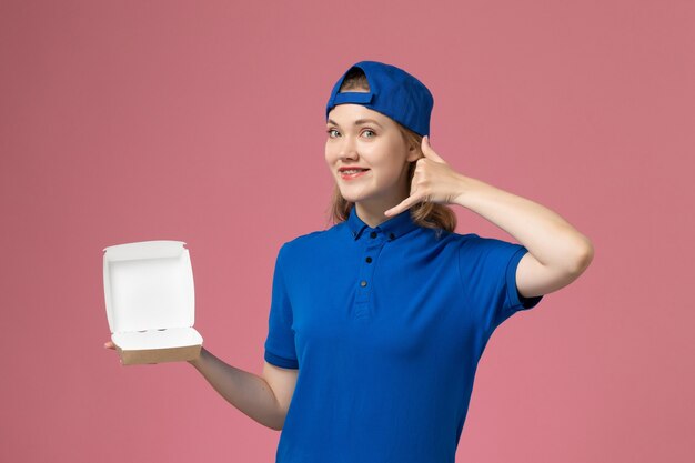 Corriere femminile di vista frontale in uniforme blu e mantello che tiene poco pacchetto di cibo di consegna su sfondo rosa dipendente di lavoro di servizio uniforme di consegna del lavoro