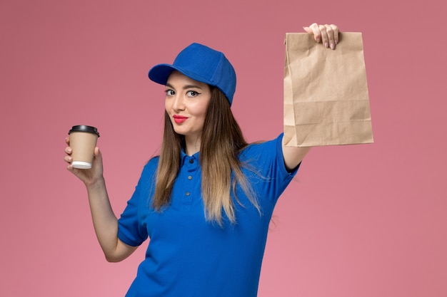 Corriere femminile di vista frontale in uniforme blu e pacchetto dell'alimento della tazza di caffè di consegna della tenuta del capo sulla parete rosa