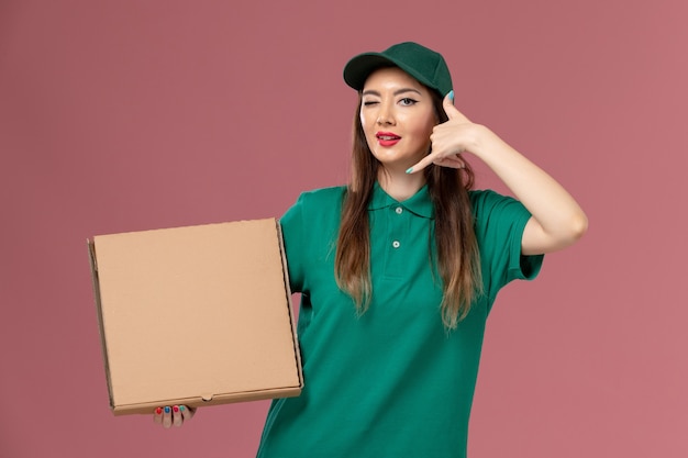 Corriere femminile di vista frontale nella scatola dell'alimento della tenuta dell'uniforme verde sulla consegna uniforme di servizio dell'operaio di lavoro della parete rosa