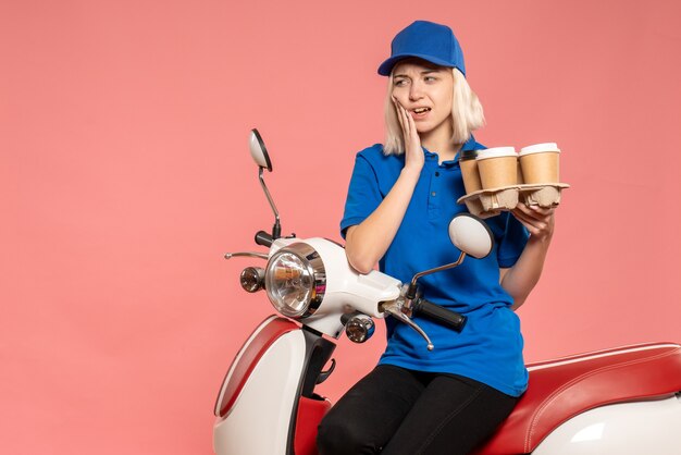 Corriere femminile di vista frontale sulla bici con le tazze di caffè sulla rosa