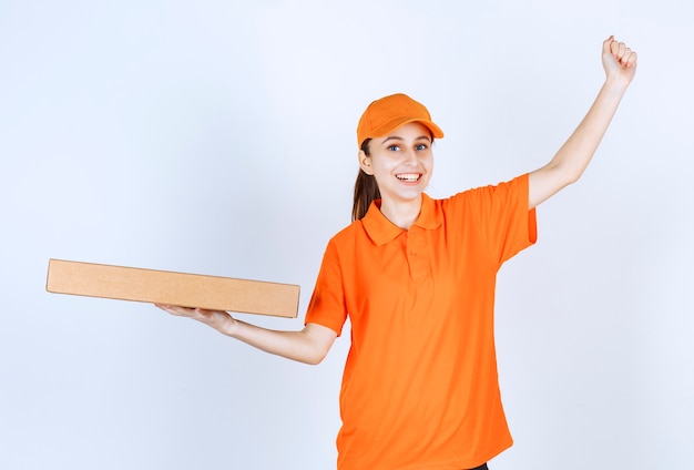 Corriere femminile in uniforme arancione che tiene una scatola di pizza da asporto e mostra il suo pugno