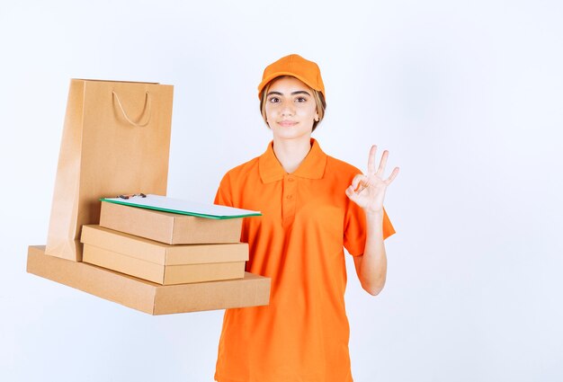 Corriere femminile in uniforme arancione che tiene una scorta di pacchi di cartone e borse della spesa e si gode la qualità del servizio