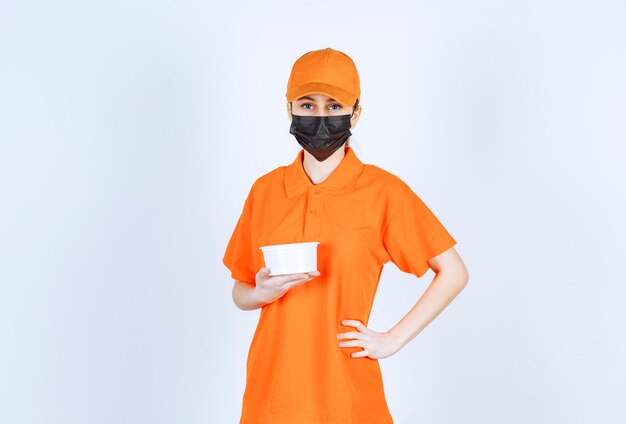 Corriere femminile in uniforme arancione e maschera nera che tiene un bicchiere di plastica