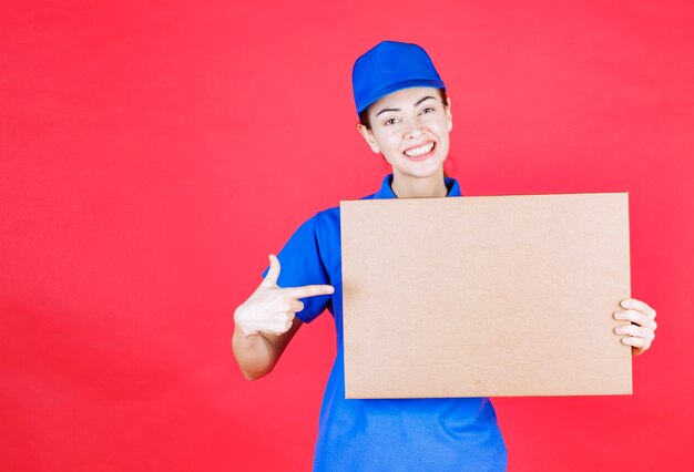 Corriere femminile in uniforme blu che tiene in mano una scatola di cartone per pizza da asporto.