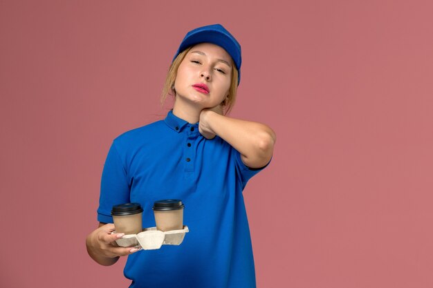 corriere femminile in uniforme blu che tiene tazze di caffè con mal di collo in rosa, lavoro di consegna uniforme di servizio